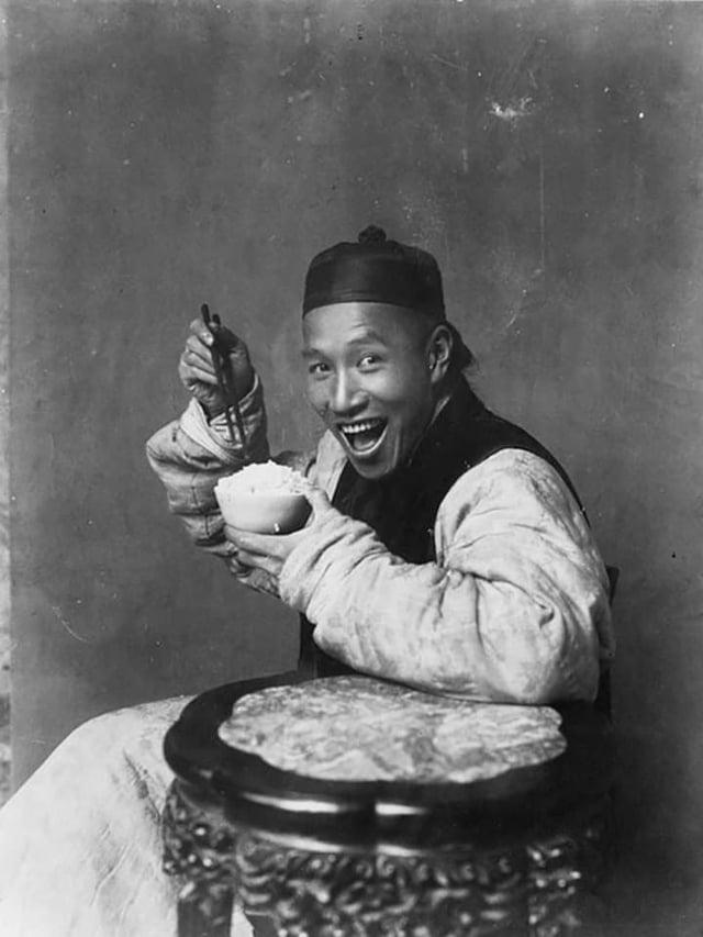 a Chinese man grins with his mouth open, posing with a bowl of rice and chopsticks