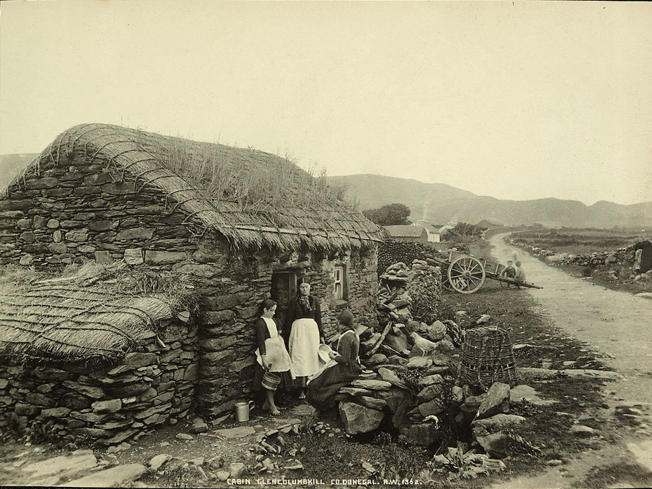 a woman and a girl stand in front of a stone house with a thatched roof.