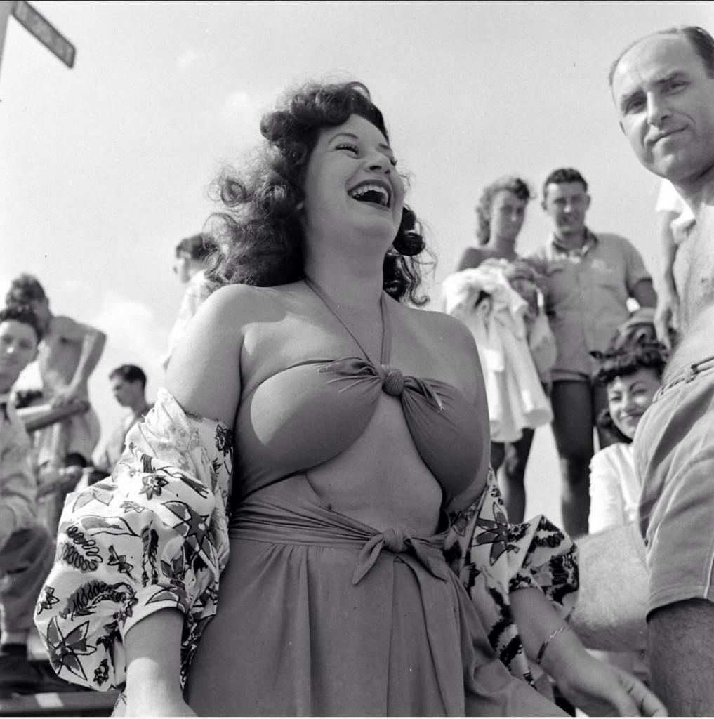 amid a group of people, a woman wearing a bathing suit laughs